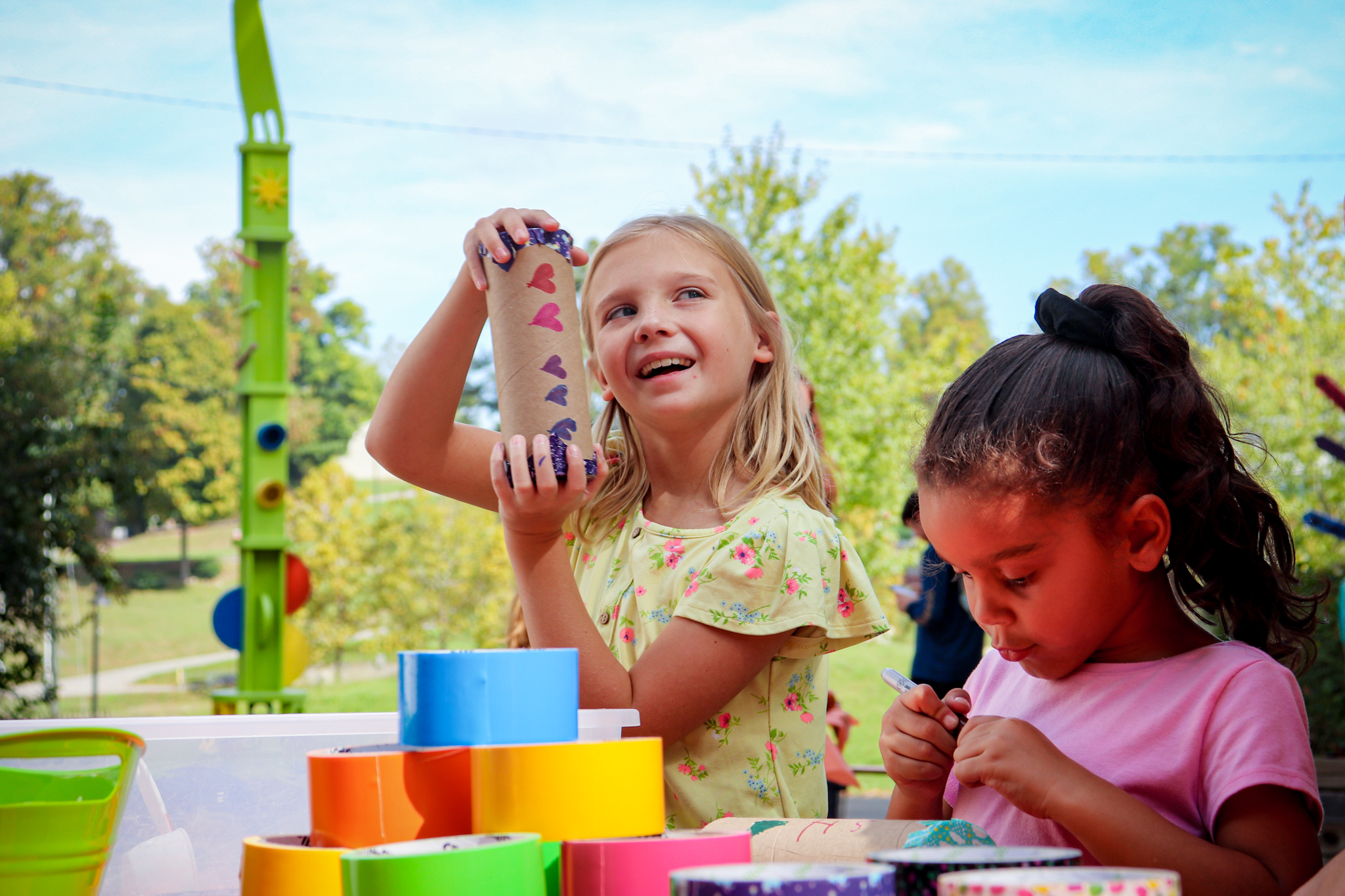 Two young girls are playing with a paper roll craft outside