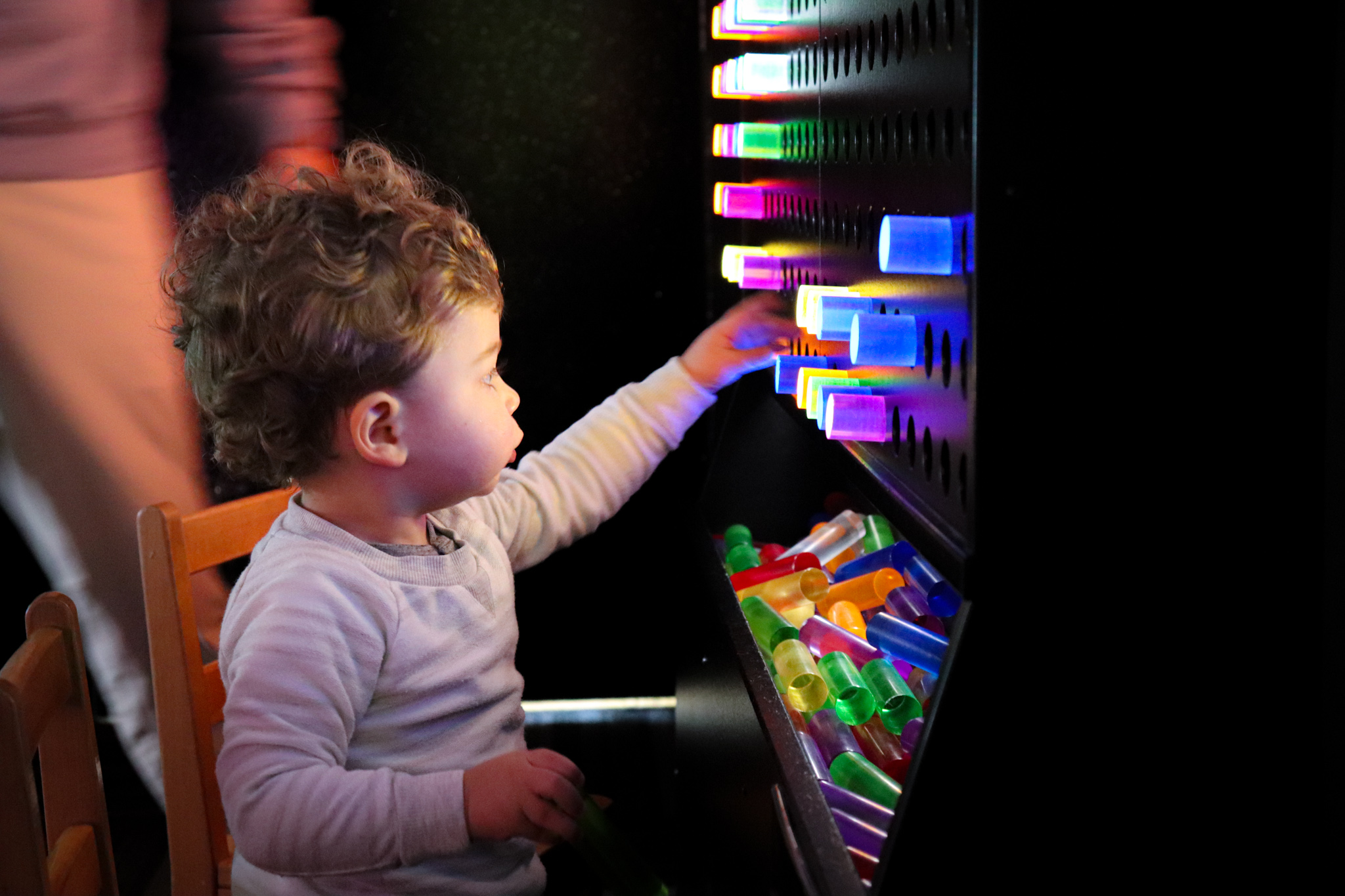 A toddler-aged child is playing with a colorful light toy, similar to Lite Brite but larger.