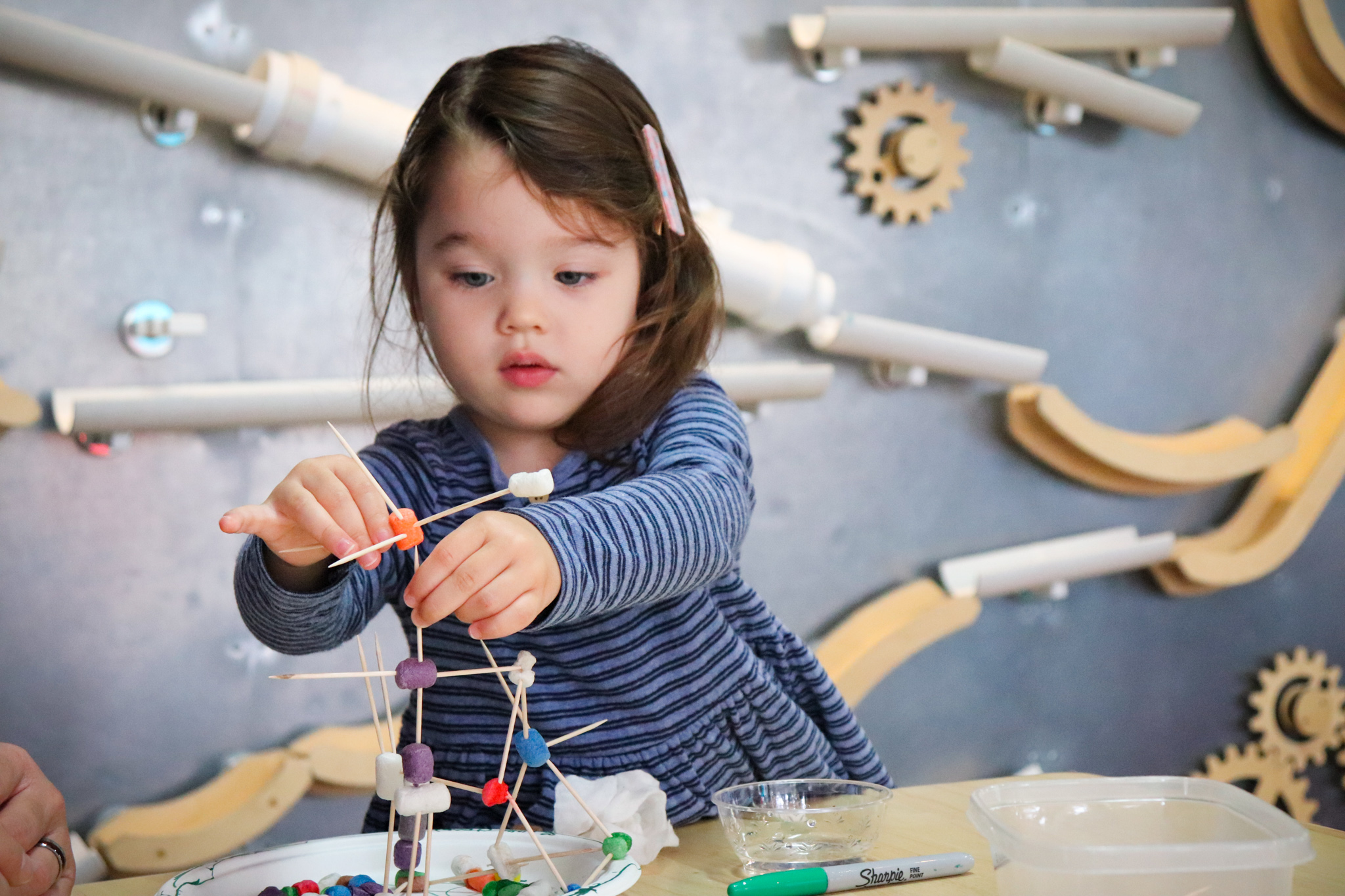 A young girl with brown hair is playing with a toothpick craft