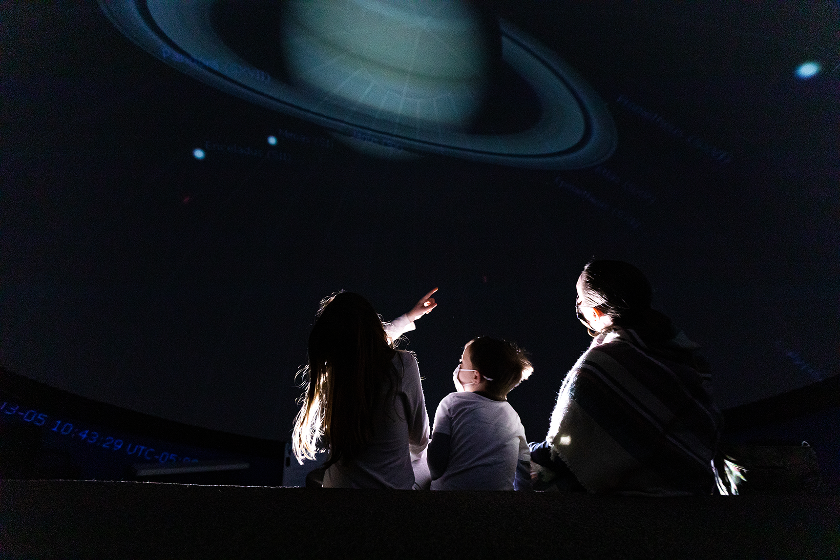 A photo of an adult and two children from the back inside a planetarium