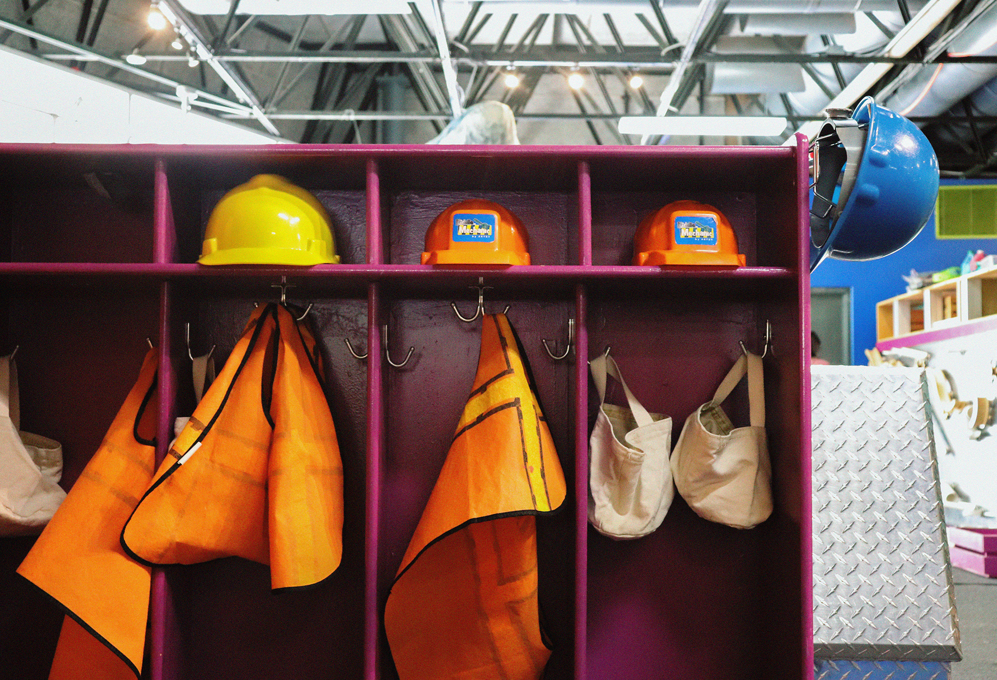 Cubbies with hangers with small play hard hats and safety vests hanging up at Muse Knoxville
